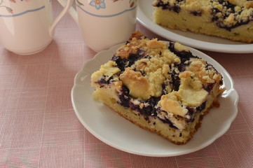 Grandma's homemade yeast cake made with frozen berries and crumble on white plate with two lovely mugs
