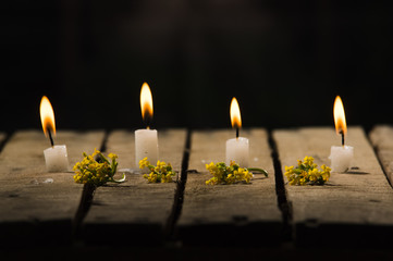 Four white wax candles sitting on wooden surface burning with black background, beautiful light...