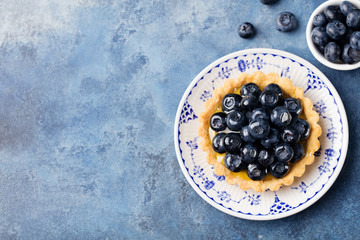 Blueberry tartlet, pie, tart with vanilla custard. Blue stone background. Top view Copy space