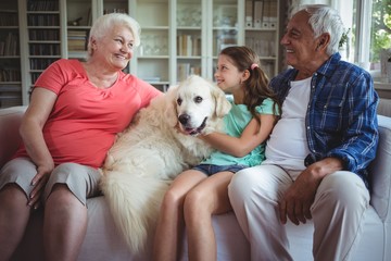 Grandparents and granddaughter sitting on sofa with pet dog