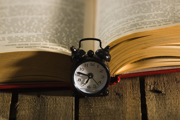 Thick book lying open on wooden surface, old fashioned night table clock sitting next to it, magic concept shoot