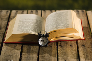 Thick book lying open on wooden surface, old fashioned night table clock sitting next to it, magic...