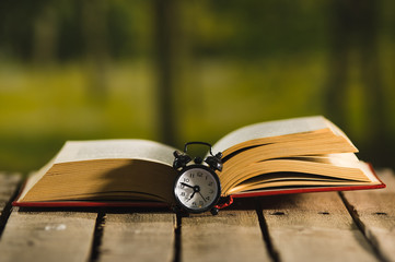 Thick book lying open on wooden surface, old fashioned night table clock sitting next to it, magic...