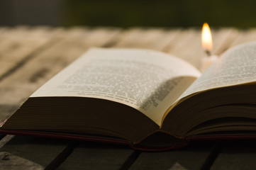 Thick book lying open on wooden surface, wax candle sitting next to it, beautiful night light setting, magic concept shoot