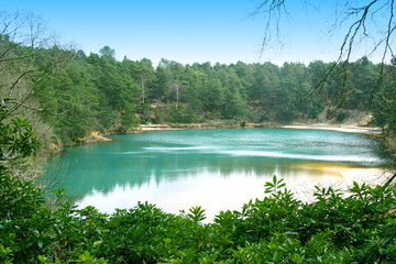 The Blue Pool - a turquoise lake in a reserve in Dorset, England, with gorse bushes in the foreground and pines in the background