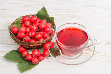 Гроздь боярышника, ягоды в корзине и чашка чая из боярышника на деревянном фоне