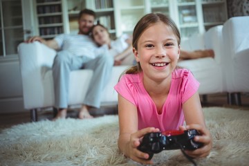 Smiling girl lying on rug and playing video game in living room