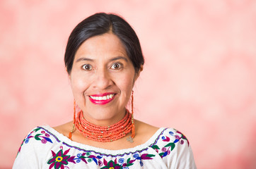 Headshot beautiful hispanic mother wearing traditional andean clothing, posing happily while smiling to camera, pink studio background