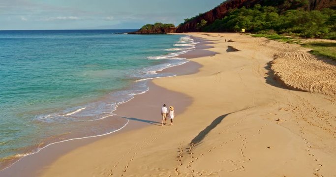 Aerial view of happy retired couple walking down the beach, vacation retirement concept