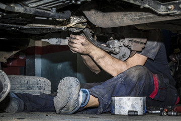 Mecánico reparando la trasmisión y los frenos de un coche en el taller. Reparación de vehículos. Revisión y mantenimiento. Cambio de neumáticos. 