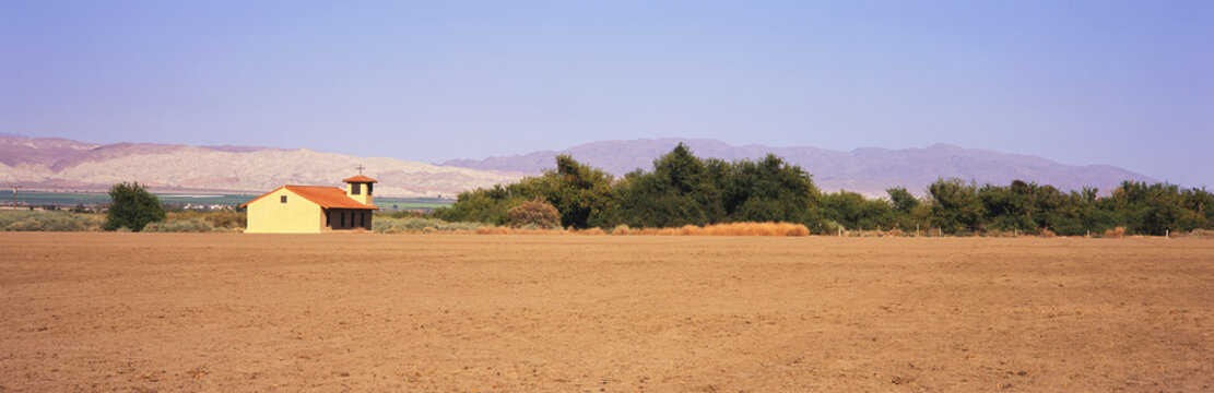 A fallow field lies in the foreground with a country church, green fields and mountains beyond, Santa Ynez Valley, Lompoc, California, United States of America