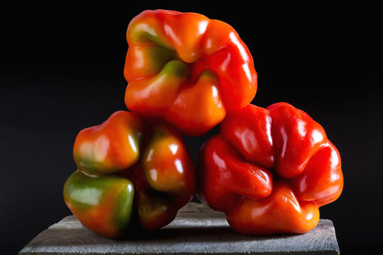 Close up of the bottoms of three colourful and interesting shaped red/green peppers on top of each other on a wooden board and black background, Calgary, Alberta, Canada