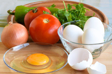 White eggs, a cracked egg, tomato, onion, green pepper are ready for cooking meal. Egg yolk in a plate. 