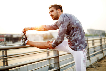 Male runner doing stretching exercise, preparing for sunset workout