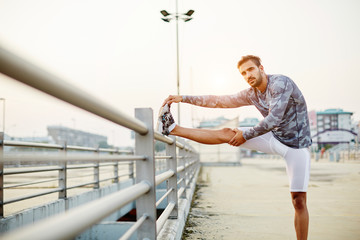 Male runner doing stretching exercise, preparing for sunset workout