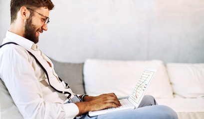 Happy young man, wearing glasses and smiling, as he works on his laptop to get all his business done early in the morning