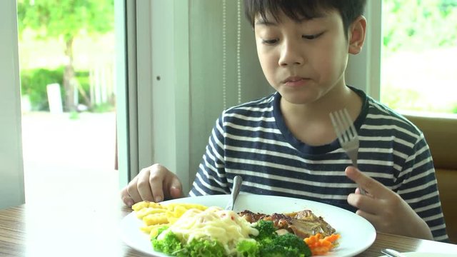 little Asian boy eating steak with vegetable Salad at restaurant with smile face