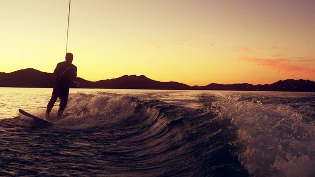 A man wake boards from boat on lake at sunset.