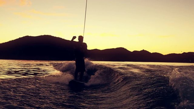 A man wake boards from boat on lake at sunset.