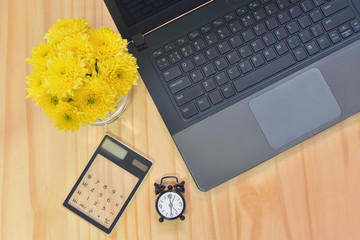 Top view laptop and calculator on wooden working table with the soft focus of yellow Chrysanthemum flower