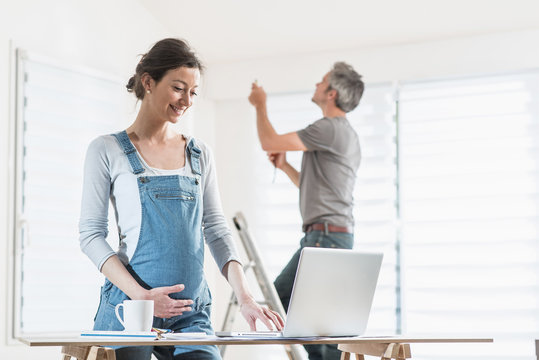 A cheerful couple expecting a child performs works in the house