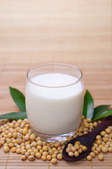 Soy milk in clear glass decorated by green leaf and soybean on wooden spoon with bamboo background.