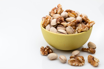 Pistachios and walnuts in a bowl on white background.