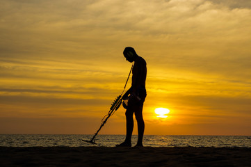 Treasure hunter with Metal detector on sunset the beach