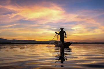 Fototapeta na wymiar Silhouette fisherman on fishing boat setting net with sunrise