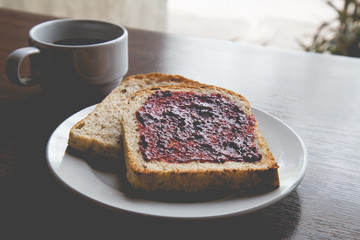 Bread with strawberry jam, and hot coffee on a wooden table. Pic