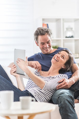 Cheerful couple sitting on a white couch at home using a tablet