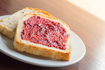 Bread with strawberry jam, and hot coffee on a wooden table.