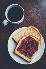 Bread with strawberry jam, and hot coffee on a wooden table. Pic