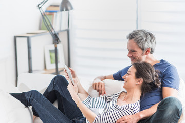 Cheerful couple sitting on a white couch at home using a tablet