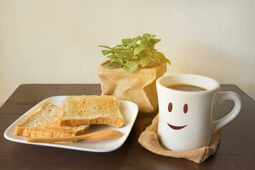 Smile of latte coffee with bread and sunshine on wooden background.