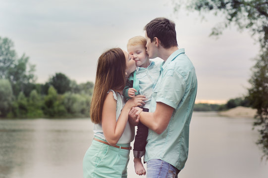 Family - mom and dad kissing son on the cheek on the banks of the river, the sunset time, turquoise clothes.