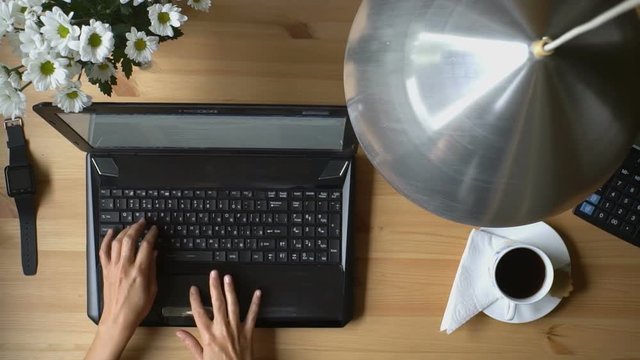 
A woman working at a computer with smart watches, coffee and bouquet of flowers on the table. Top view. Slow motion.