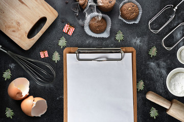 A blank clipboard with kitchen utensils and  christmas toys on black background, copy-space.