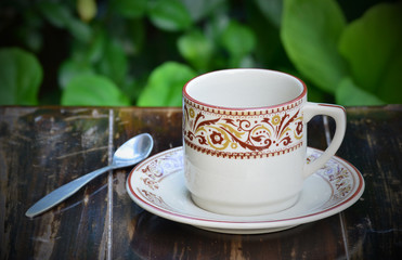 A cup and spoon on a wooden table with green background.