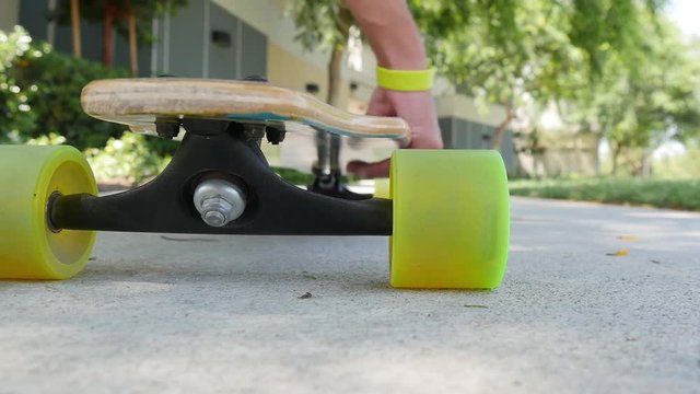 A slow motion low angle shot of a teenager picking up his skateboard and walking away.