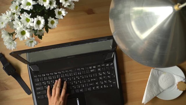 
A woman working at a computer with coffee and bouquet of flowers on the table. Top view. Dolly shot.