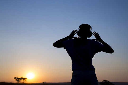Silhouette young woman with headphone on sunrise background.
