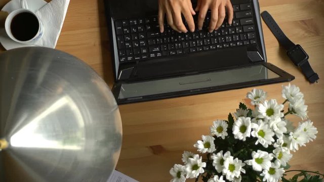 A woman working at a computer with coffee and bouquet of flowers on the table. Top view. Dolly shot.