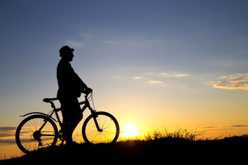 Fototapeta premium Silhouette of sports person cycling on the field on the beautifu