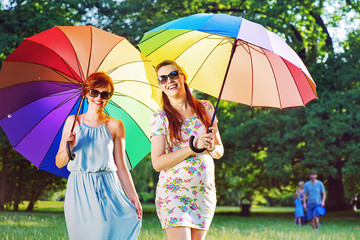 Two fashionable young women posing with colorful umbrellas