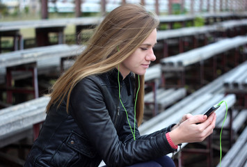 Young beautiful girl look and listening music on your mobile phone  the old stadiums bench