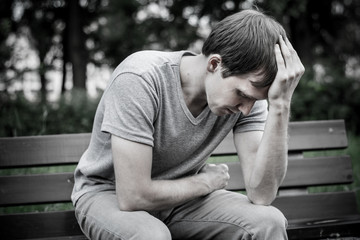 A man sits on a bench. He is sad and pensive.
