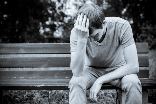 A man sits on a bench. He is sad and pensive.

