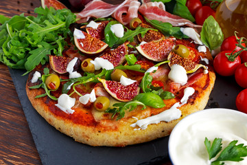 Fig pizza with bacon, green pimiento olives, rocket and basil leaves