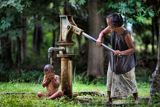 The old woman pumping a water pump to bathe small children.